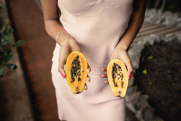Cropped view of trendy young african american woman in summer dress holding fresh cut papaya while standing in garden center, fashion-forward lady inspired by tropical plants, concept d'été - Photo, image