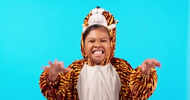 Tiger costume, roar and face of girl in studio with halloween onesie for fun, playful and playing. Childhood, blue background and portrait of child with crazy, goofy and silly expression for scare. - Footage, Video