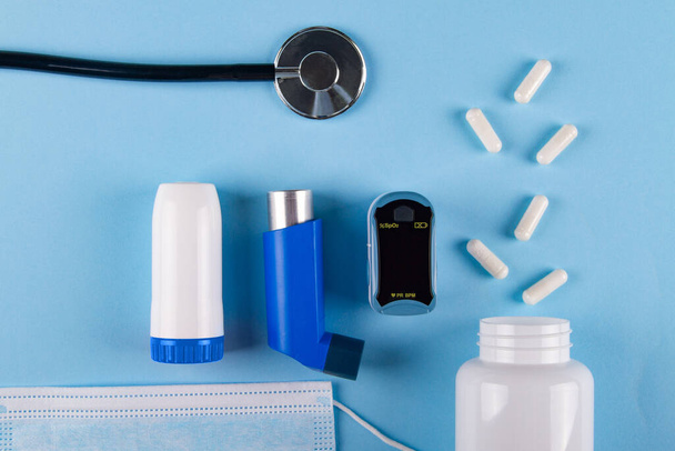 医療用マスク、聴診器、酸素濃度計、錠剤のボトルとコピースペースと青の背景に吸入器のトップビュー。喘息による胸部圧迫感の概念 - 写真・画像