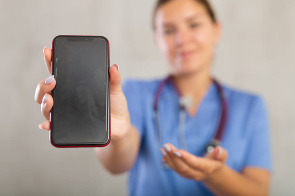 Young positive woman in medical uniform posing in studio with mobile phone - Foto, Bild
