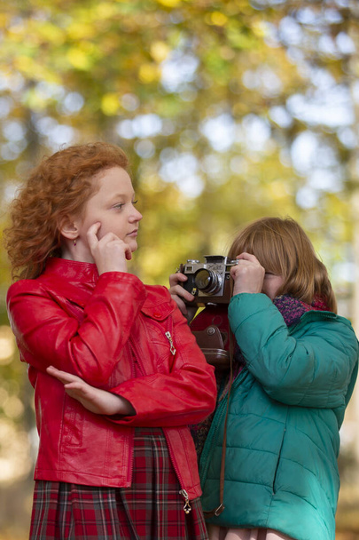 Dos chicas de pelo rojo novias se fotografían en el parque de otoño con una cámara retro. - Foto, imagen