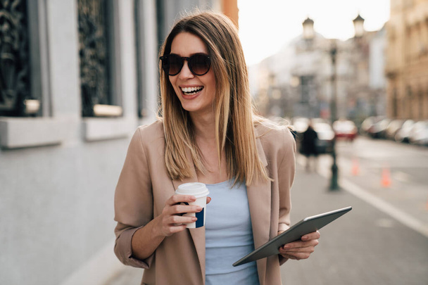 Attractive young successful woman drinking a coffee and using a digital tablet while enjoying break - Φωτογραφία, εικόνα
