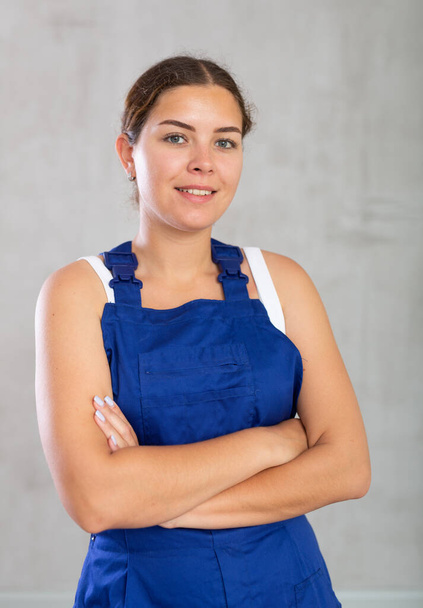 Portrait of young woman builder or mechanic in blue protective overalls on a gray background - Foto, Bild