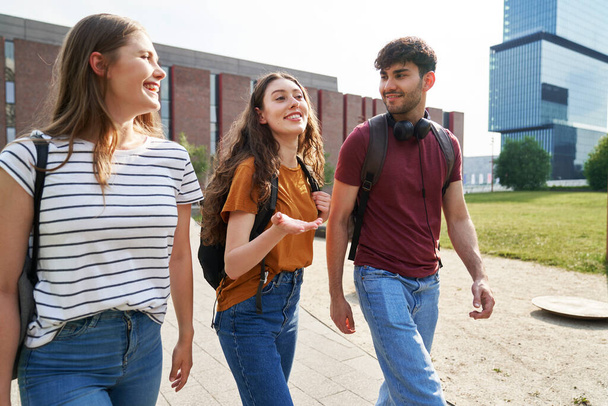 Gruppe von drei kaukasischen Studenten läuft durch den Universitätscampus  - Foto, Bild