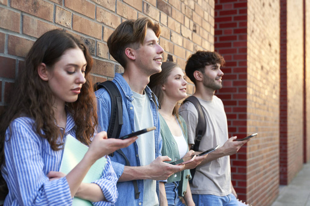 University students browsing phones next to university campus building - Photo, Image