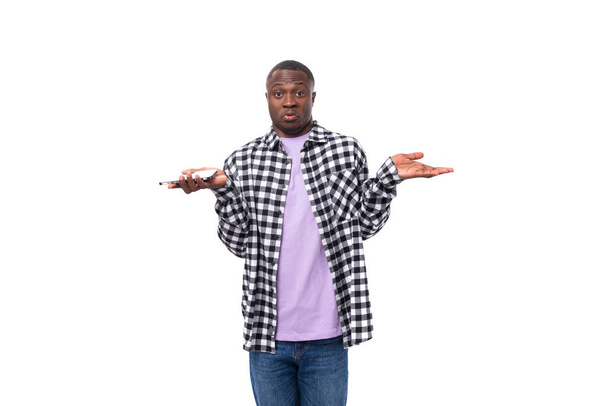 un homme africain confus de 30 ans vêtu d'une chemise à carreaux noir et blanc hausse les épaules sur le fond avec un espace de copie. - Photo, image