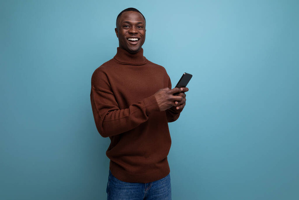 счастливый молодой африканский фрилансер, работающий удаленно, используя смартфон и онлайн-соединение на фоне студии с копировальным пространством. - Фото, изображение