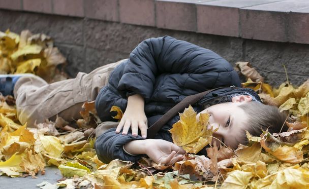 A happy child lies in the autumn leaves in the city. Warm autumn. - Photo, Image
