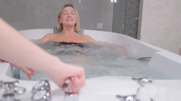 A satisfied blonde lies in a hot tub with warm bubbles. Spa procedures. Relaxation of luxurious people - Záběry, video