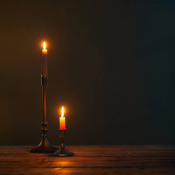 burning candles in vintage candlesticks on dark background - Foto, afbeelding