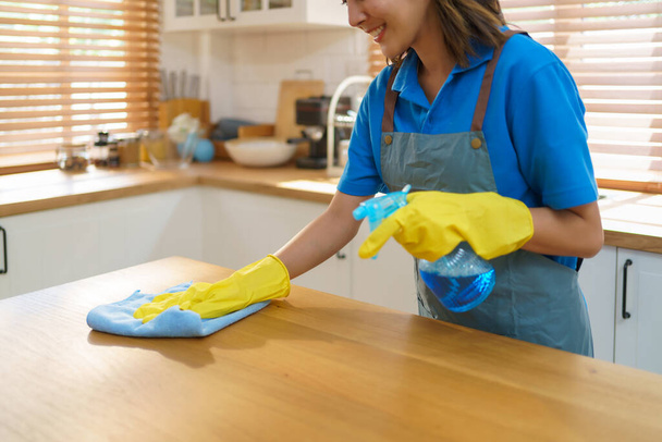 Geschickte asiatische Hausfrau nutzt mühelos Tischdecke und Sprayer in ihrer Küche und demonstriert ihre Kompetenz bei der Schaffung eines sauberen und einladenden Raums für ihre Familie. - Foto, Bild