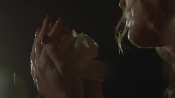 Zblízka pohled na romantickou ženu ve tmě noci držící bílou růži, něžné štíhlé ruce. Být zamilovaný, snít a čekat na rande. Blonďatý model k nepoznání. Vysoce kvalitní 4K záběry - Záběry, video