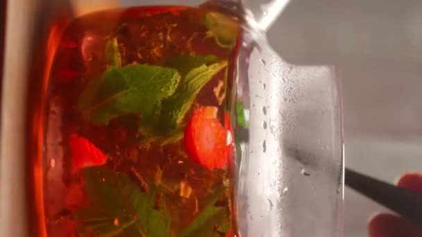 Process of brewing tea, tea ceremony, freshly brewed fruit and herbal tea. Spoonful stirs tea in teapot with tea leaves, mint, strawberries and fruit in glass teapot on table. close-up. - Footage, Video