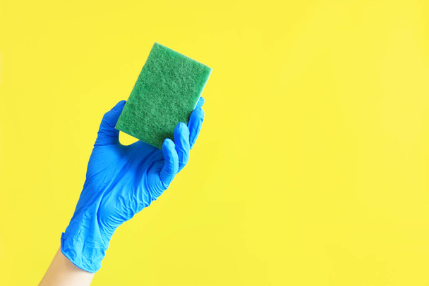 Ręka kobiety w rękawiczce trzyma gąbkę do zmywania naczyń. Sprzątanie domu. Ręka z zieloną gąbką na żółtym tle. Czyszczenie reklam - Zdjęcie, obraz