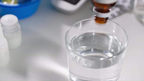 una mujer gotea gotas médicas de la botella con un dispensador para normalizar la presión en un vaso de agua, de cerca - Imágenes, Vídeo