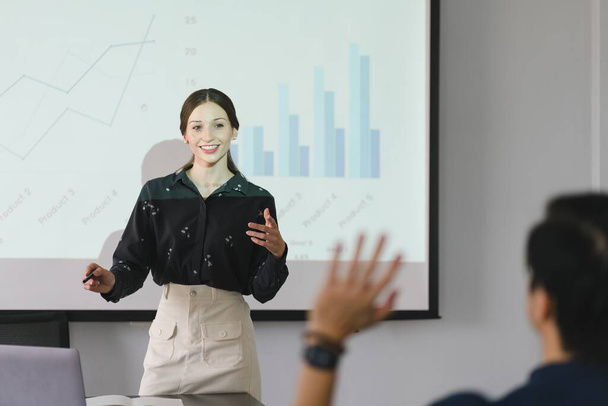 Kadın analist, bir grup ekonomist için bir toplantı sunumu yapıyor. Projektör ekranında grafikler, ürün satışları, gelir büyüme stratejileri ve e-ticaret analizleri gösteriliyor. - Fotoğraf, Görsel