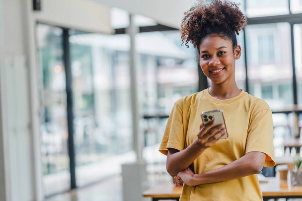 Portret van een gelukkige jonge Afro-Amerikaanse vrouw die vol zelfvertrouwen lacht met een smartphone. afro-Amerikaanse zakenvrouw het lezen van een sms-bericht op haar mobiele telefoon - Foto, afbeelding