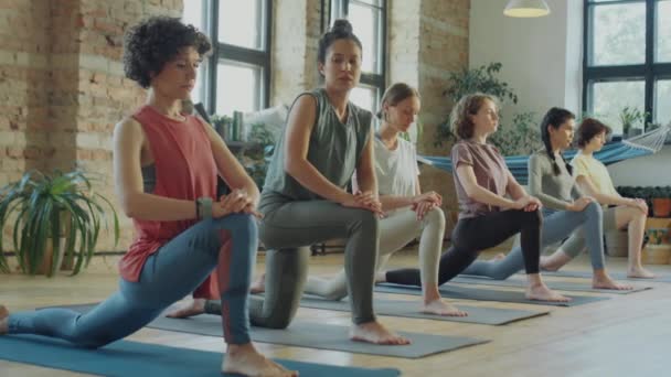 Instructora de fitness femenina y grupo de mujeres haciendo embestida y estiramiento de corredor durante el entrenamiento de yoga en estudio - Metraje, vídeo