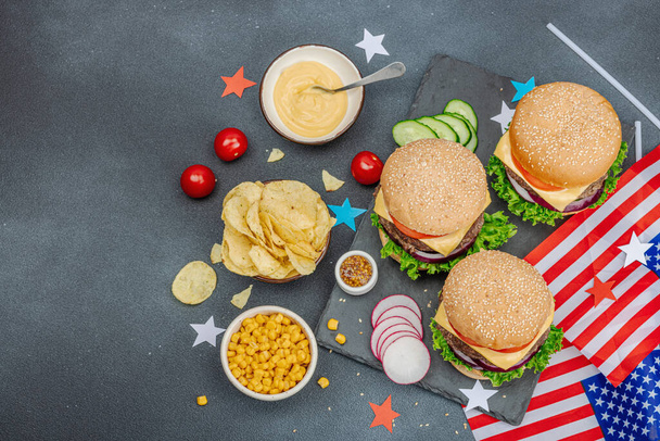 Homemade burgers. An American classic, traditional food for picnic, party or celebration Independence Day. Sauce, chips, sweet corn. Dark stone concrete background, top view - Foto, Imagen