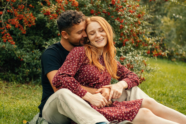Giovane bella coppia seduta su erba nel parco durante l'estate e abbracciando. - Foto, immagini