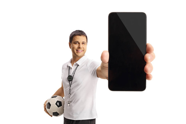 Entraîneur de football tenant un ballon et montrant un smartphone isolé sur fond blanc - Photo, image