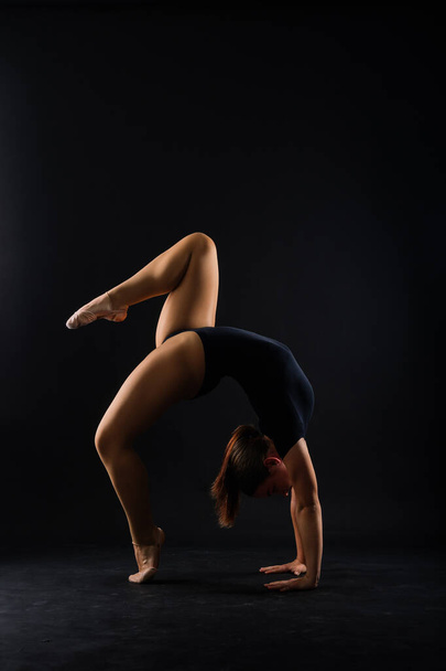 A girl gymnast in a swimsuit does tricks on white and dark background. Front view - Fotografie, Obrázek