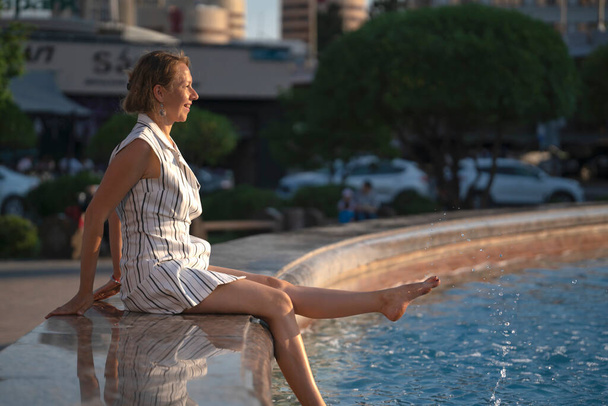 Portrait of a young blonde woman who sits at the city fountain. High quality photo - Photo, Image