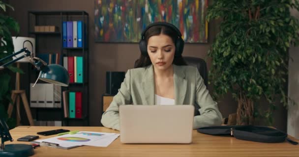 Female office workes sits at table in office at home dream job for lady. Buisness time work online from distance. Lady wears headphones has video conference with coleagues after hard working day. - Filmagem, Vídeo