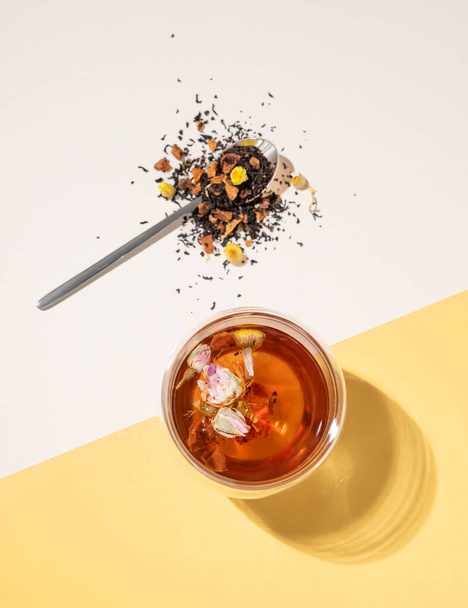 Pose créative plate d'une tasse en verre de tisane avec des fleurs de rose sur un fond jaune et blanc avec une ombre dure. Concept de nourriture et boissons. Vue du dessus et espace de copie. - Photo, image