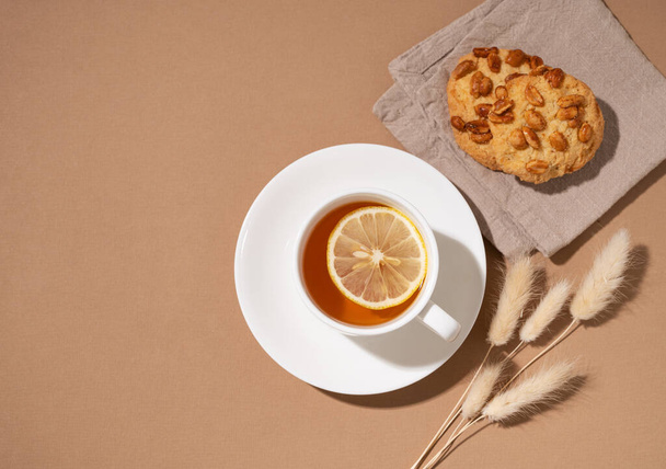 Une tasse de thé avec du citron et des biscuits faits maison sur une serviette sur un fond brun. Concept de boisson saine et confortable. Vue du dessus et espace de copie. - Photo, image