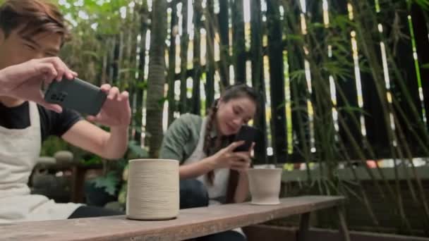 Giovane asiatico uomo e donna scattare foto di vasi di argilla con smartphone su ceramica masterclass - Filmati, video