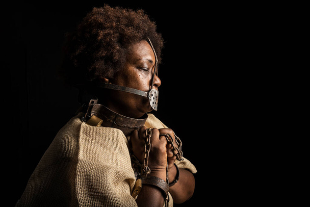 Portret czarnej kobiety z łańcuchami na rękach i żelazną maską na twarzy reprezentującej niewolnicę Anastacię. Niewolnictwo w Brazylii. - Zdjęcie, obraz