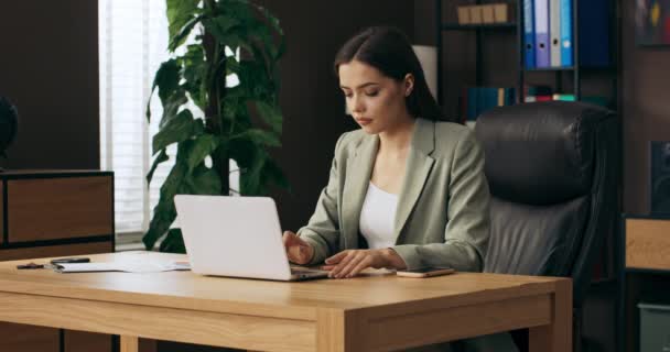 Vrouw in buisness pak zitten aan stoel werkt online vanuit huis voelt zich opgelucht en gemotiveerd ontspannen na hard werken houdt schoffel in de hand en benen op het bureau . - Video