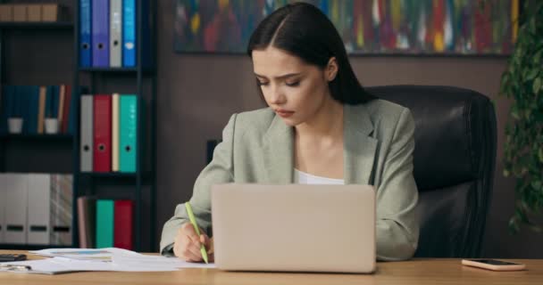 Young woman in buisness suit sits at table at office from home taping on keyboard write notes takes call from coleagues . - Materiał filmowy, wideo