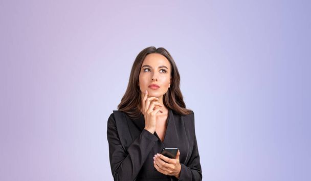 Femme d'affaires réfléchi lever les yeux avec téléphone à la main, vide espace de copie fond violet. Portrait pensif, recherche d'informations et de nouvelles idées. Concept de plan et de choix - Photo, image