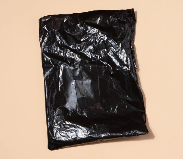 Bolsa de plástico negro sobre fondo beige, vista superior - Foto, imagen