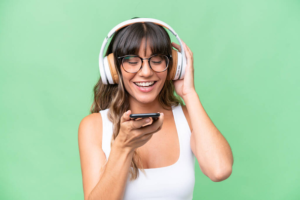 Giovane donna caucasica su sfondo isolato ascoltare musica con un cellulare e cantare - Foto, immagini