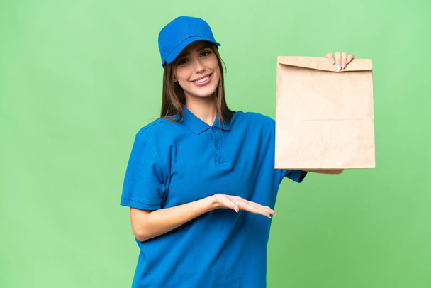Νεαρή όμορφη καυκάσια γυναίκα παίρνει μια σακούλα φαγητό από το πακέτο πάνω σε απομονωμένο φόντο απλώνοντας τα χέρια στην άκρη για την πρόσκληση να έρθει - Φωτογραφία, εικόνα