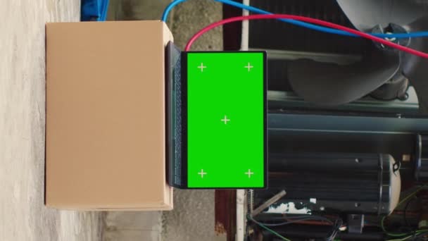 垂直ビデオ屋外エアコンの前に緑の画面のラップトップ。プロのメンテナンスを必要とする壊れた外部HVACシステムの横にクロマキーガジェットのディスプレイをモックアップ - 映像、動画