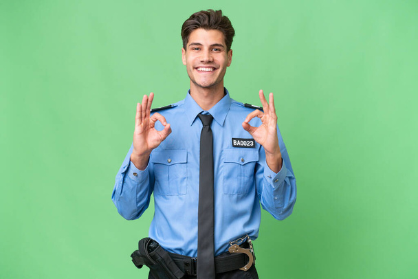 Young police man over isolated background showing an ok sign with fingers - Photo, Image