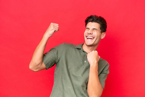 Young caucasian handsome man isolated on red background celebrating a victory - Foto, afbeelding