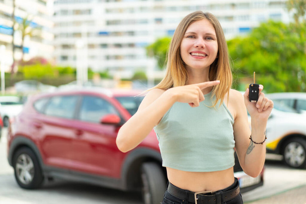 Young blonde woman holding car keys at outdoors and pointing it - Fotografie, Obrázek