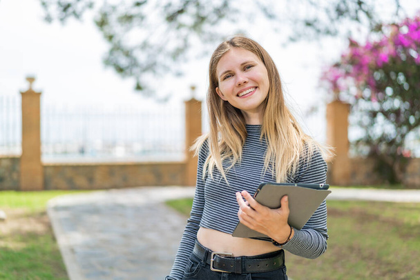 Giovane donna bionda che tiene un tablet all'aperto sorridendo molto - Foto, immagini