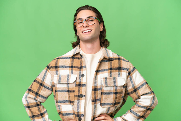 Jeune homme caucasien isolé sur fond de chroma vert posant avec les bras à la hanche et souriant - Photo, image