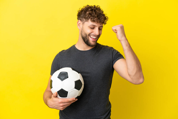 Όμορφος νεαρός ποδοσφαιριστής απομονωμένος σε κίτρινο φόντο γιορτάζει μια νίκη - Φωτογραφία, εικόνα
