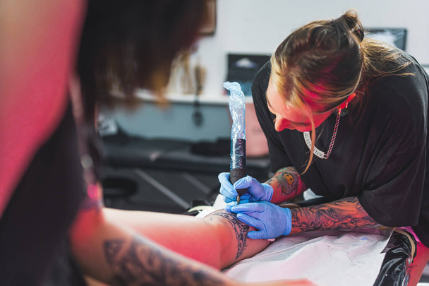 tattoo master painting human body with a needle machine, making tattoo in professional salon. High quality photo - Photo, Image