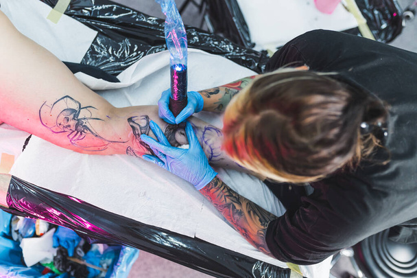 πάνω προς τα κάτω πλάνο ενός καλλιτέχνη τατουάζ κάνει μαύρο και άσπρο τατουάζ σε ένα πόδι womans. Υψηλής ποιότητας φωτογραφία - Φωτογραφία, εικόνα