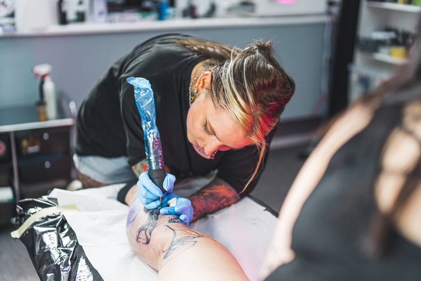 Професійна майстер-дівчина з татуювання працює над ногою клієнта в своєму салоні, середній постріл. Фотографія високої якості - Фото, зображення