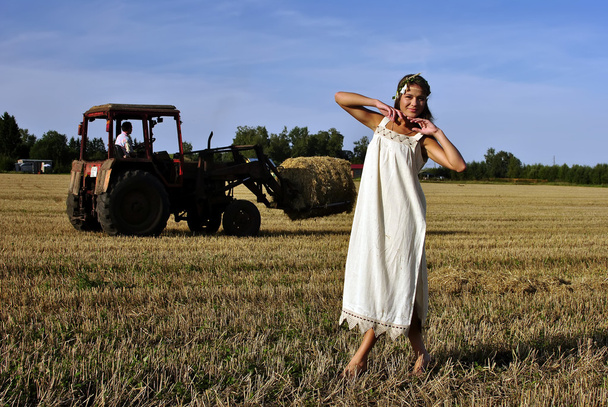 dziewczyna w wiejskich ubrania stojący na polu, ciągnik na tle - Zdjęcie, obraz