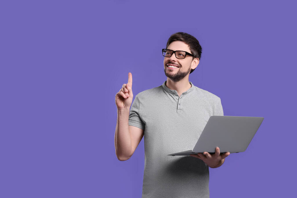 Happy man with laptop on lilac background, space for text - Fotoğraf, Görsel
